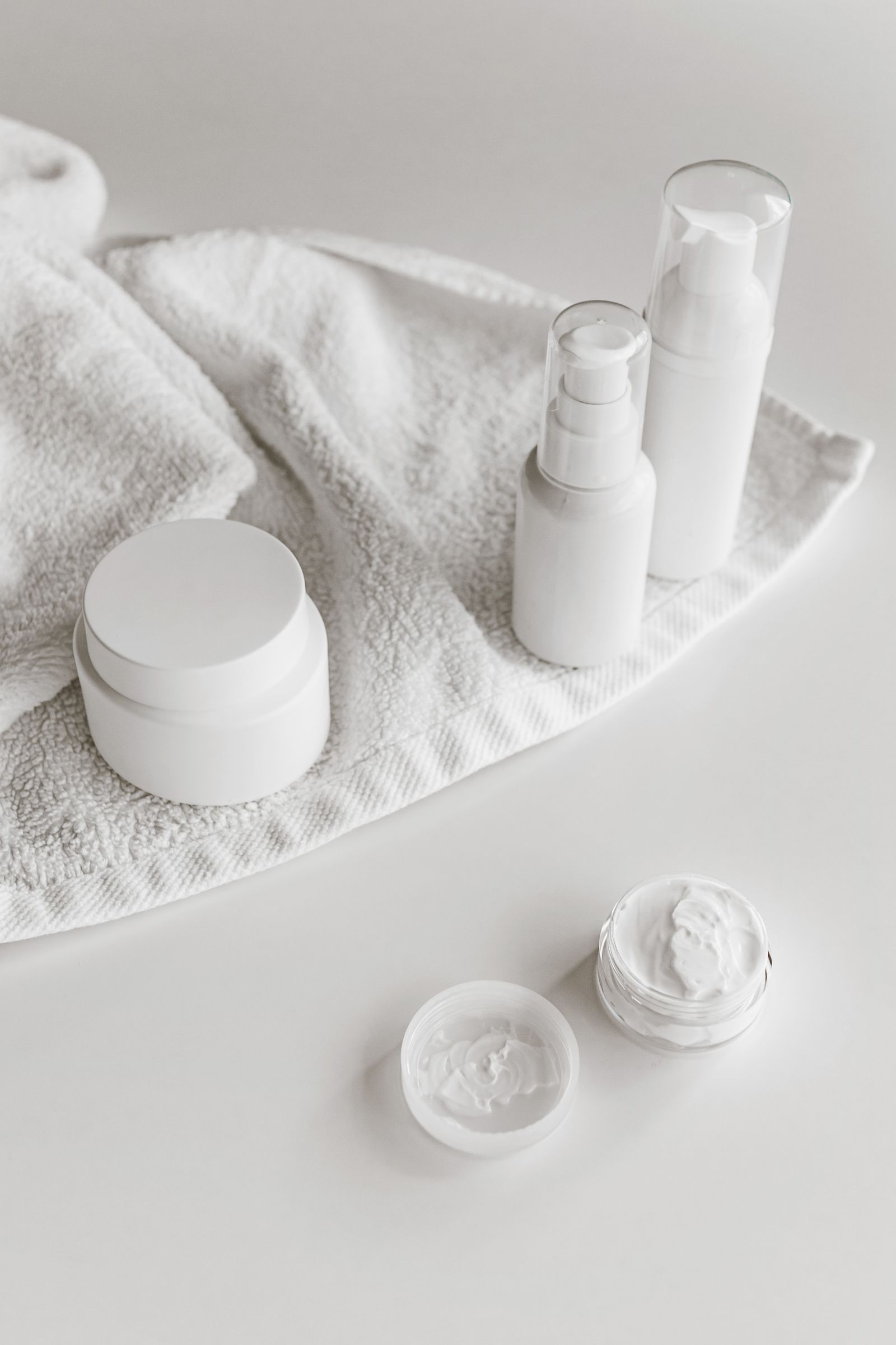 A quiet skincare still life of white bottles and cream on softly folded linen.