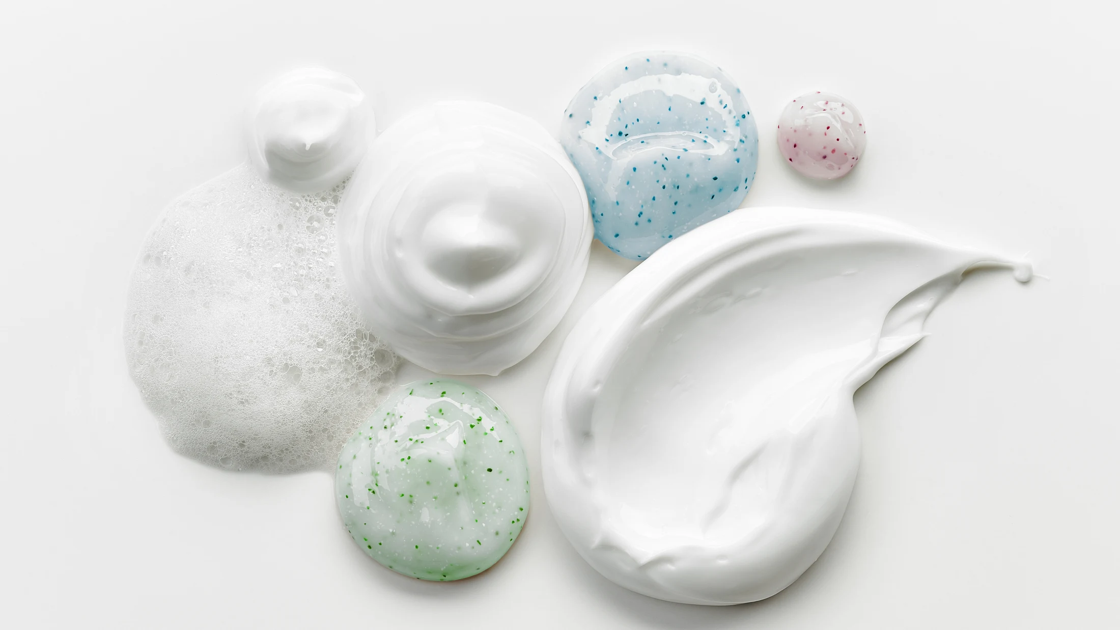 Sculptural white skincare cream, foam and delicate cleansing textures on a luminous background.