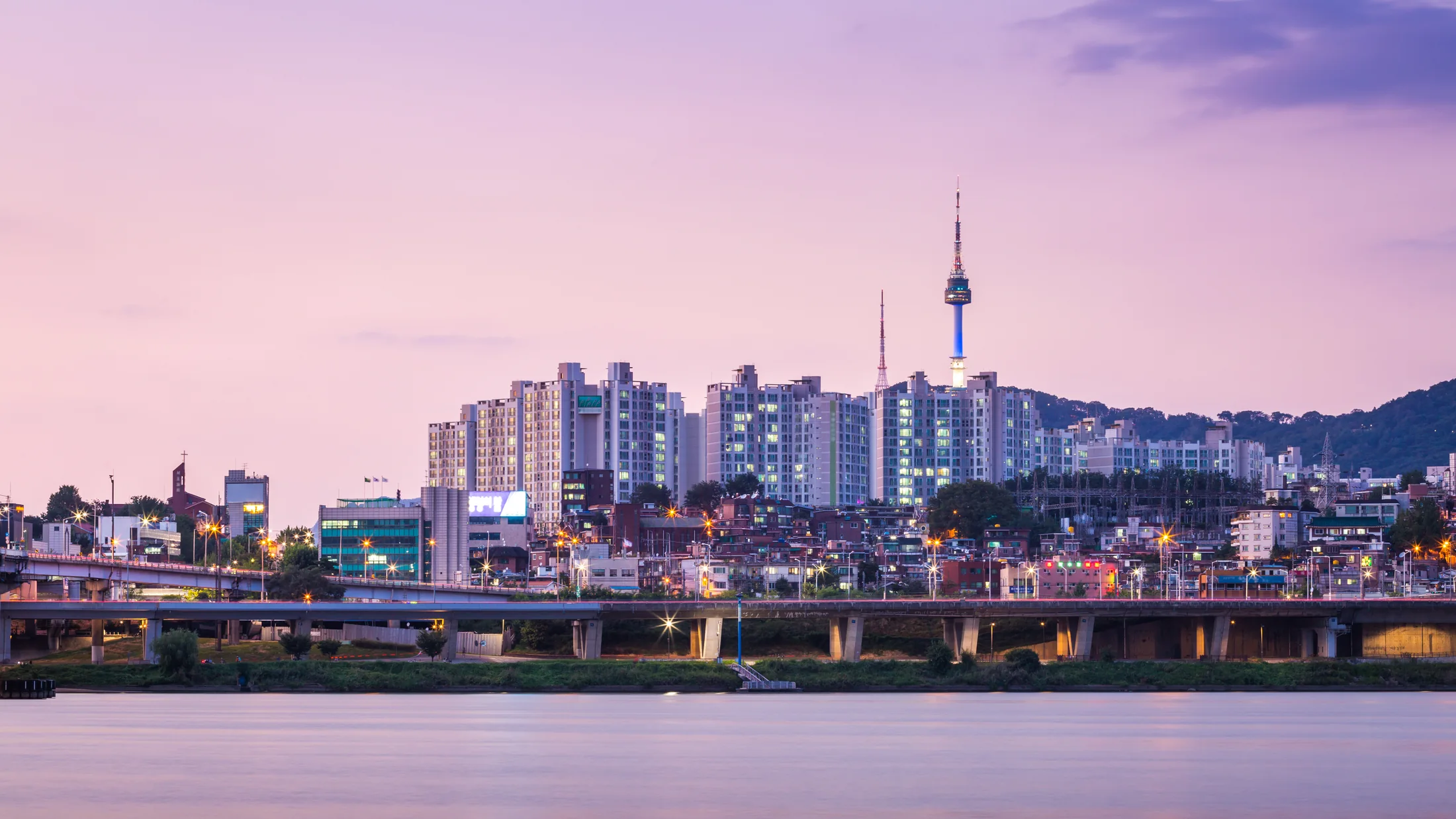 Seoul at dusk, with N Seoul Tower above the city and a river in the foreground.